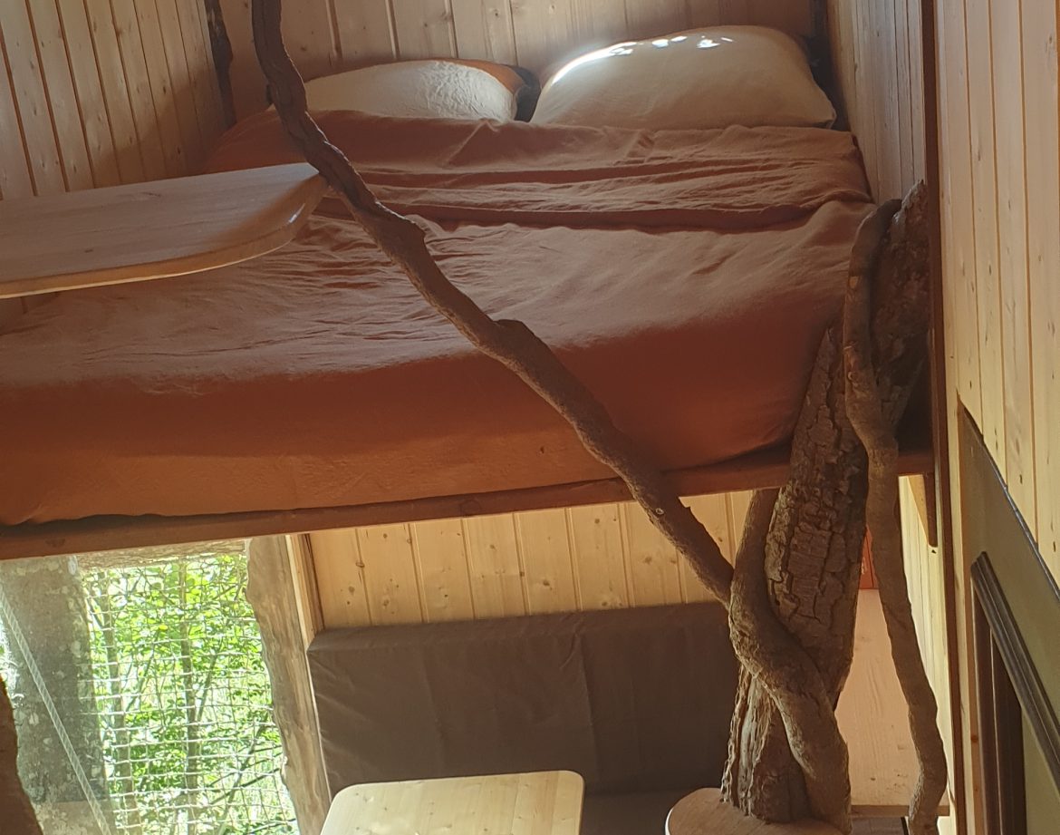Cabane perchée en bois avec un lit douillet et une vue sur la nature.