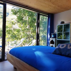 Chambre moderne avec vue sur la nature, lit bleu et balcon en Auvergne-Rhône-Alpes.