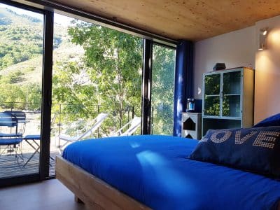 Chambre moderne avec vue sur la nature, lit bleu et balcon en Auvergne-Rhône-Alpes.