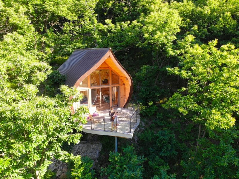 Cabane perchée en bois avec terrasse, entourée de verdure en Auvergne-Rhône-Alpes.