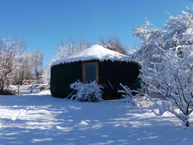 Yourte chaleureuse entourée de neige, offrant un cadre paisible et naturel.