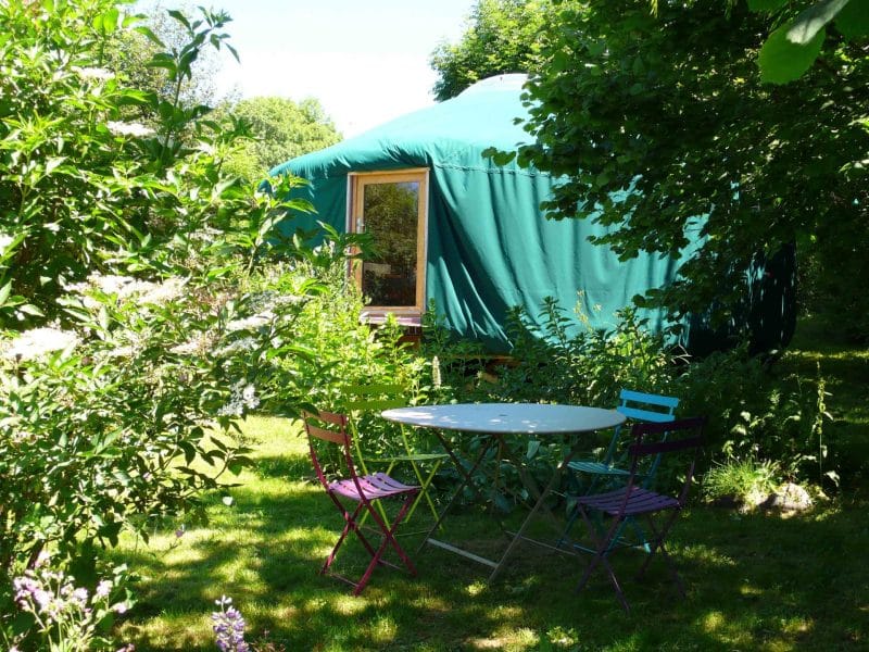 Yourte verte entourée de verdure, avec une table et des chaises colorées.