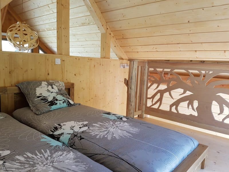 Chalet en bois avec lit jumeau et décor floral moderne. Ambiance chaleureuse et naturelle.