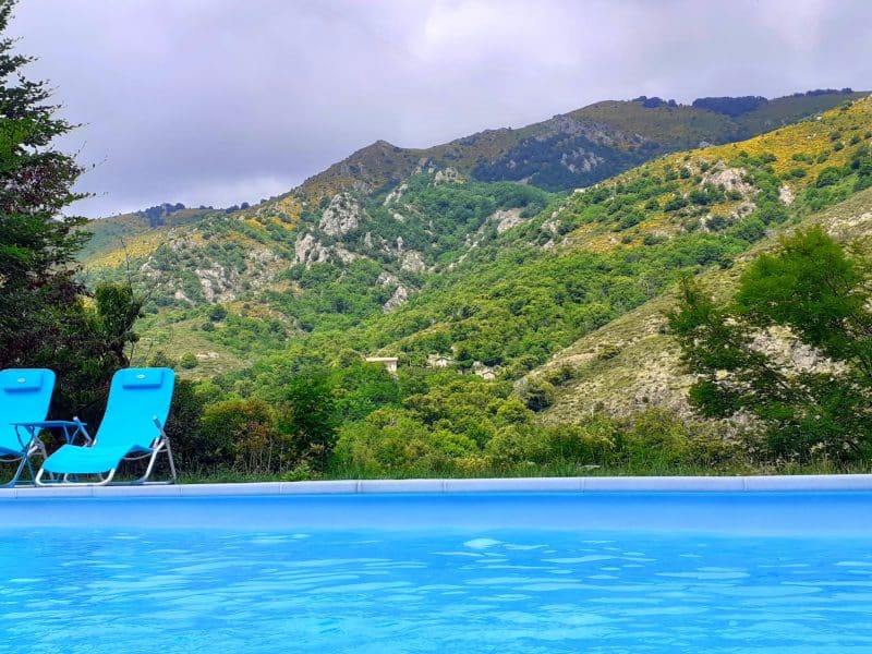 Villa avec piscine, chaises longues bleues face à une vue montagneuse verdoyante.