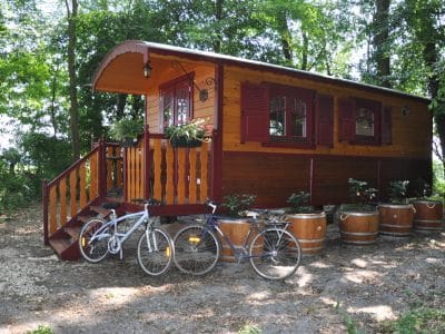 Charmante roulotte en bois entourée de verdure, avec des vélos stationnés à côté.