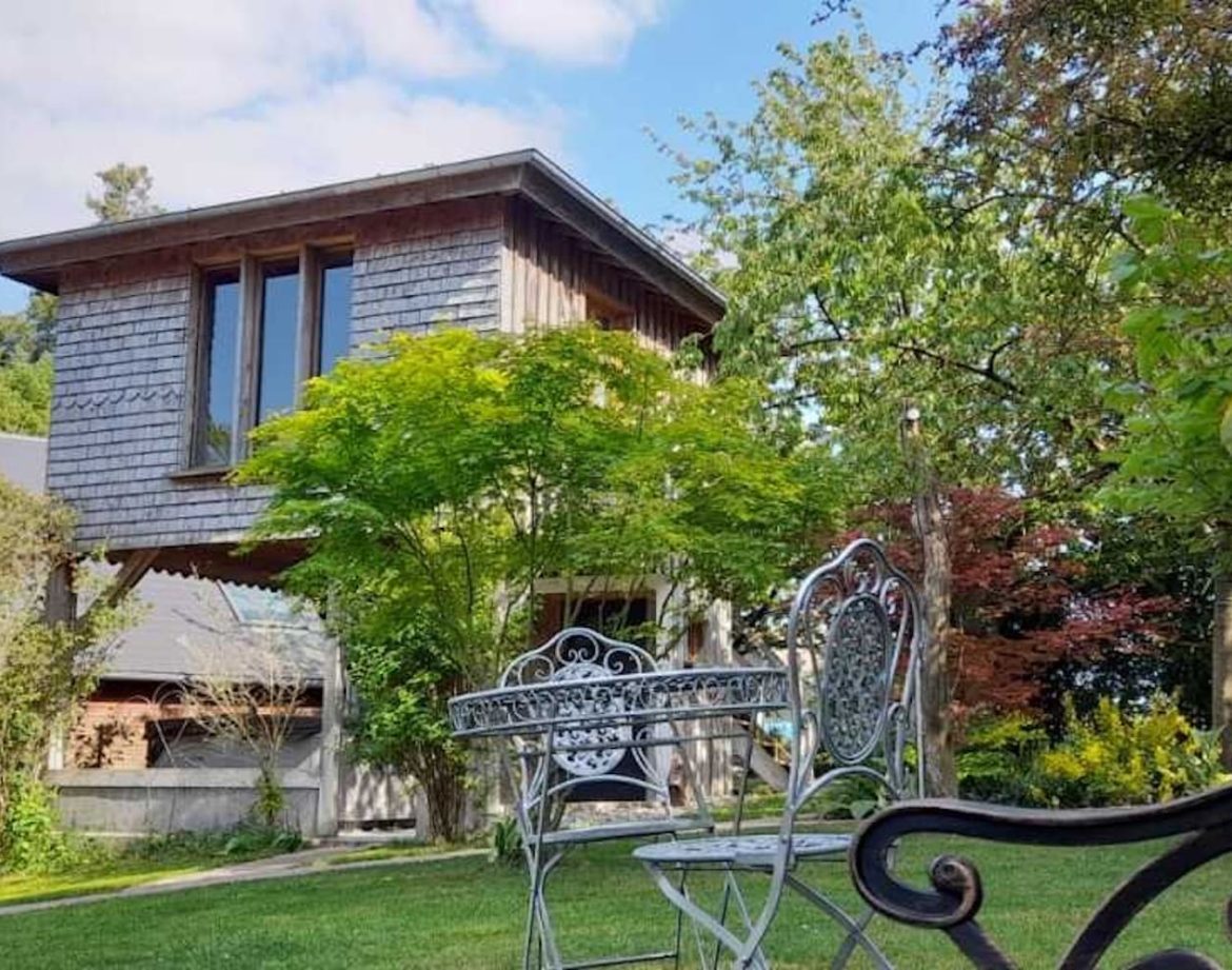 Cabane en bois dans un jardin verdoyant, entourée de chaises élégantes.