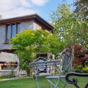 Cabane en bois dans un jardin verdoyant, entourée de chaises élégantes.