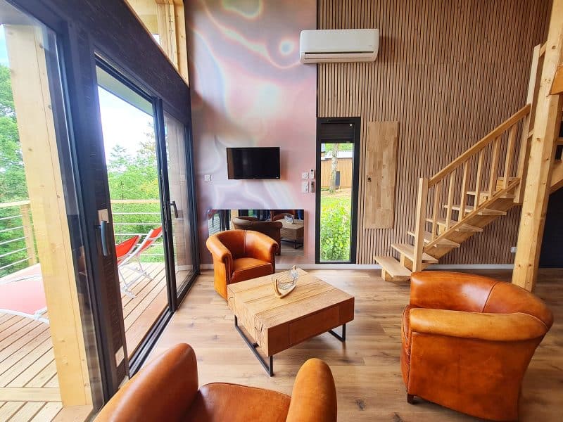 Chalet moderne avec salon lumineux et vue sur la nature, mobilier en cuir chaleureux.