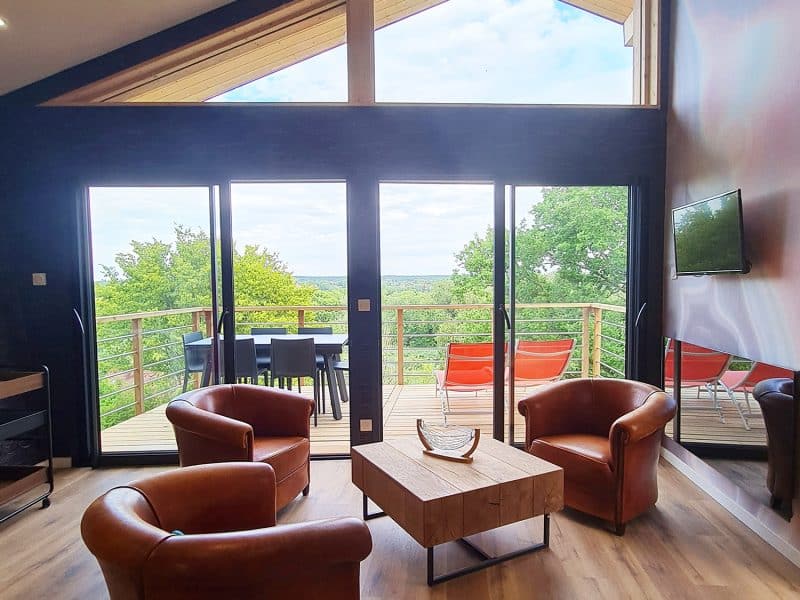 Chalet moderne avec vue panoramique, salon lumineux et fauteuils en cuir confortables.