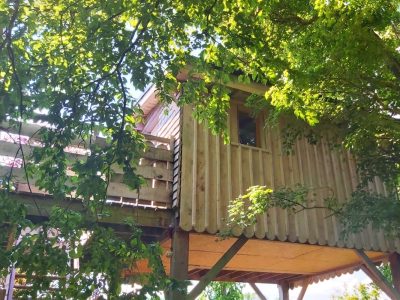 Cabane perchée en bois, entourée de verdure, offrant une vue imprenable.
