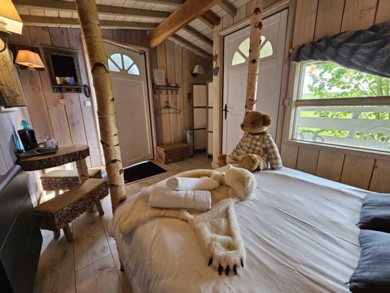Chalet chaleureux avec décor en bois, lit douillet et ours en peluche accueillant.
