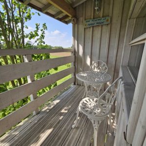 Chalet en bois avec balcon, table et chaises blanches, vue sur la nature.