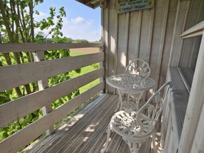 Chalet en bois avec balcon, table et chaises blanches, vue sur la nature.