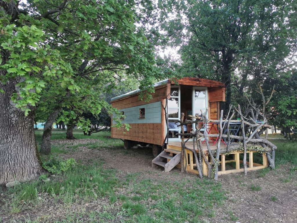 Hébergement insolite : une roulotte en bois entourée darbres verdoyants.