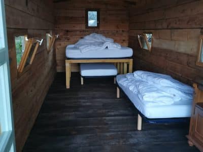 Hébergement insolite en bois, avec lits simples et fenêtres pour une vue sur la nature.