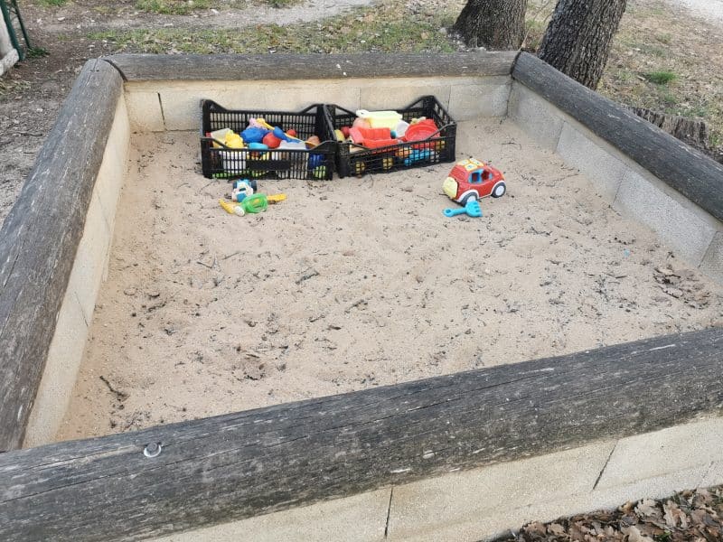 Aire de jeux en plein air avec bac à sable et jouets colorés pour enfants.