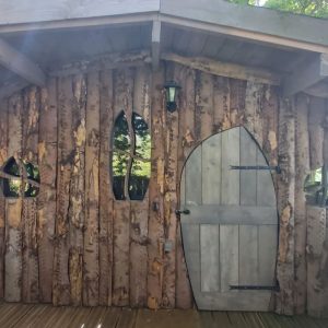 Cabane en bois dans les arbres, avec des fenêtres en forme darc et une porte en bois.