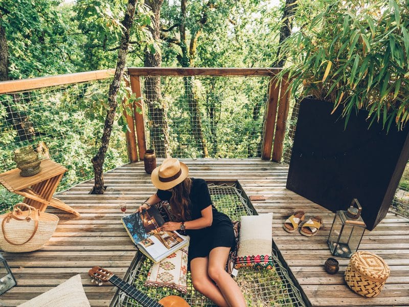 Cabane perchée dans les arbres, avec une terrasse en bois et une vue verdoyante.