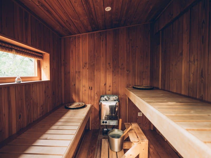 Sauna en bois chaleureux avec bancs en bois et fenêtre laissant entrer la lumière naturelle.