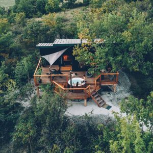 Cabane perchée en bois avec terrasse et jacuzzi, entourée de verdure à Midi-Pyrénées.