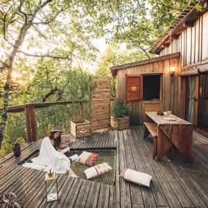 Cabane perchée en bois avec terrasse, ambiance cosy au milieu des arbres.