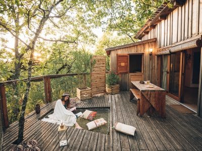 Cabane perchée en bois avec terrasse, ambiance cosy au milieu des arbres.