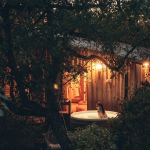 Cabane en bois avec jacuzzi extérieur, éclairée par des lanternes chaleureuses.