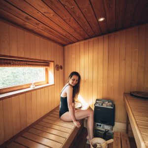 Sauna en bois chaleureux avec une femme assise, lumière douce et ambiance relaxante.