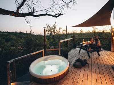 Hébergement insolite en Midi-Pyrénées avec jacuzzi sur une terrasse en bois au coucher de soleil.