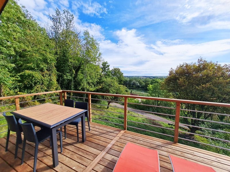 Chalet en bois avec terrasse, vue panoramique sur la nature verdoyante.
