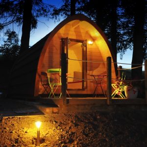 Cabane en bois à Limousin, éclairée la nuit, avec chaises colorées sur la terrasse.