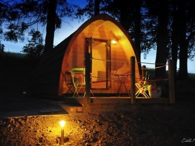 Cabane en bois à Limousin, éclairée la nuit, avec chaises colorées sur la terrasse.