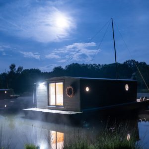 Hébergement insolite : maison flottante illuminée sur un lac au clair de lune.