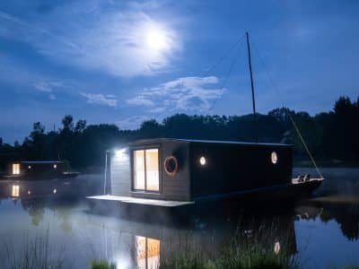 Hébergement insolite : maison flottante illuminée sur un lac au clair de lune.