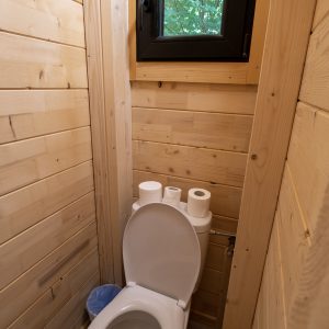 Toilettes en bois dans un hébergement insolite au Limousin, avec fenêtre sur la nature.