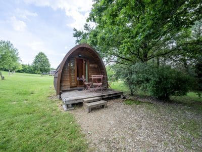 Cabane en bois en forme de dôme, avec une terrasse et un cadre verdoyant.