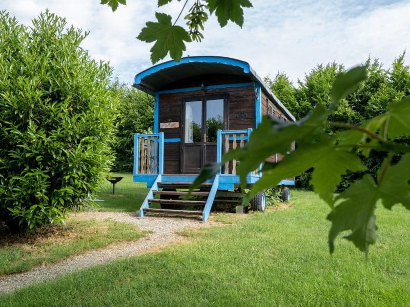 Charmante roulotte en bois avec balustrade bleue, entourée de verdure à Limousin.