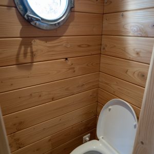 Toilettes en bois dans un hébergement insolite en Auvergne, avec hublot rond.