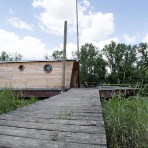 Hébergement insolite : maison flottante en bois avec fenêtres rondes, au bord de leau.