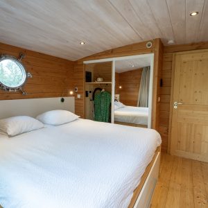 Chambre cosy en bois dans un hébergement insolite en Auvergne, avec miroir rond.