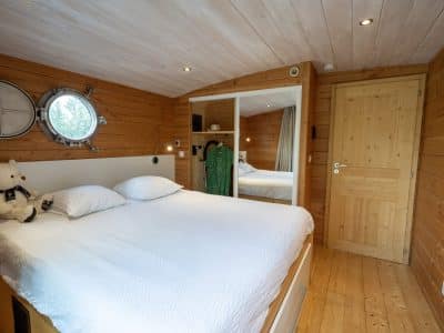 Chambre cosy en bois dans un hébergement insolite en Auvergne, avec miroir rond.