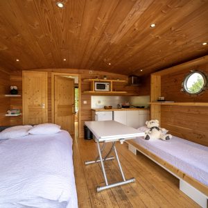 Hébergement insolite en Limousin : intérieur en bois chaleureux avec lits simples et cuisine.