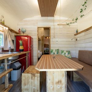Hébergement insolite en cabane, intérieur en bois avec une table en bois et un frigo rouge.