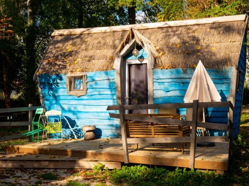 Cabane colorée en bois avec toit de chaume, située dans un cadre verdoyant.