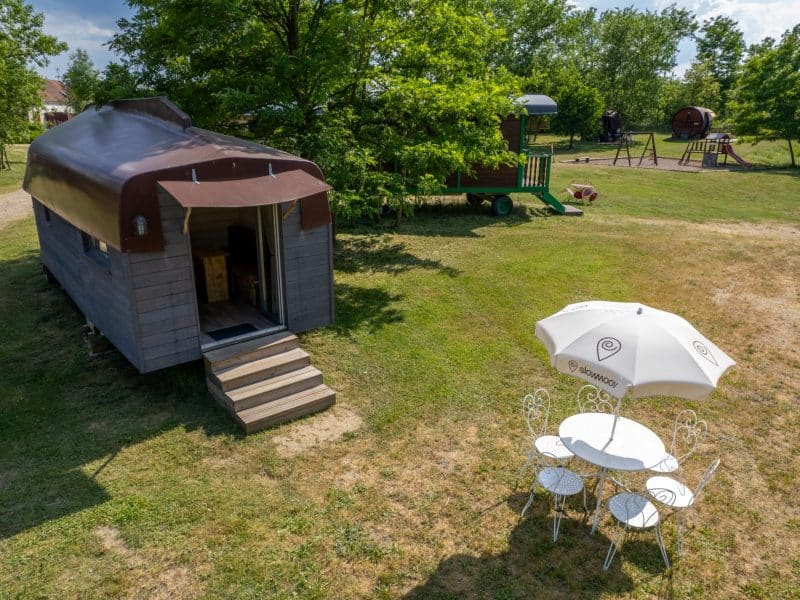 Hébergement insolite en Auvergne : roulotte en bois avec terrasse et parasol.