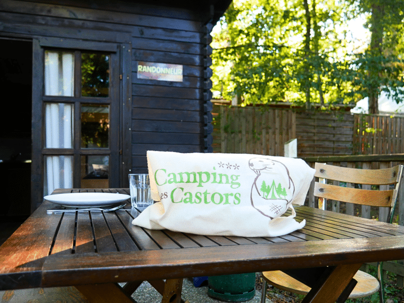 Cabane en bois à Camping les Castors, table en bois avec assiette et verre.