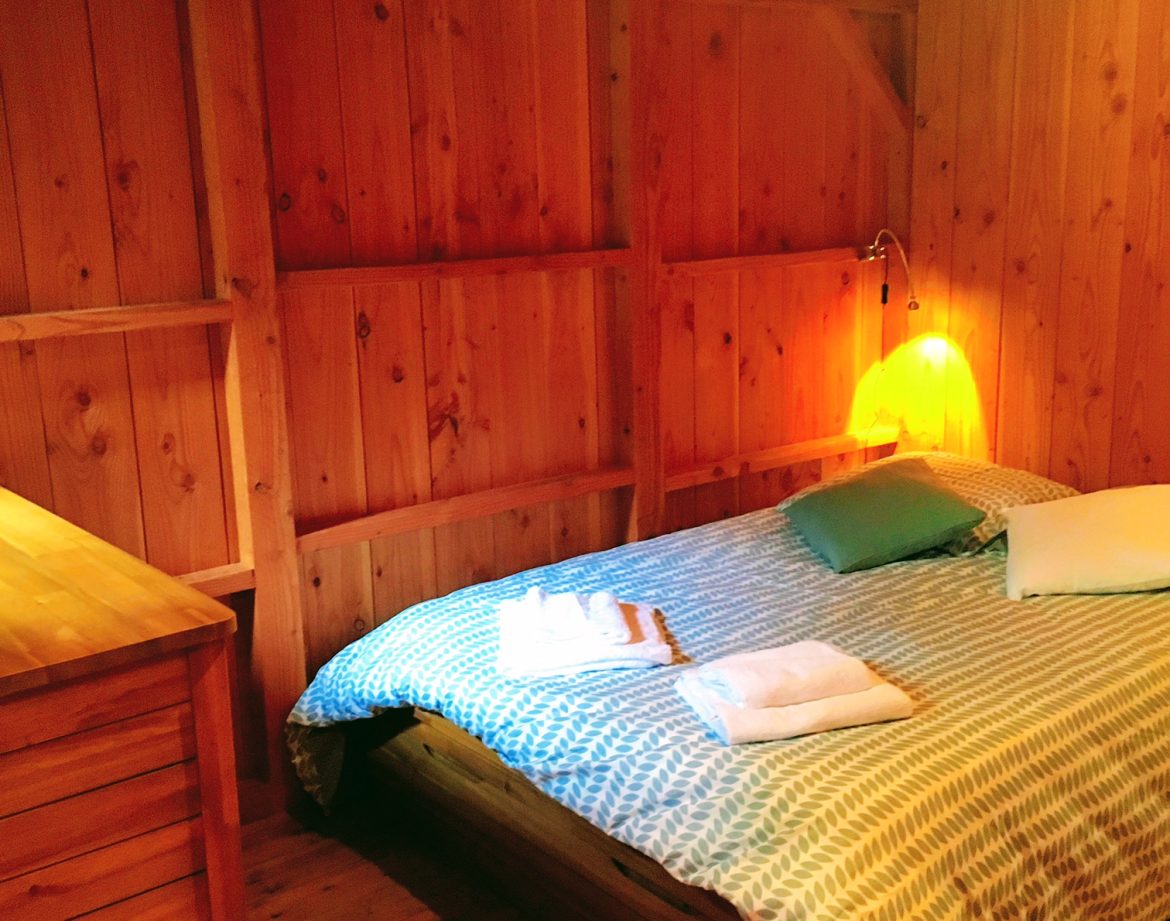 Chalet en bois chaleureux avec lit douillet et lumière tamisée.