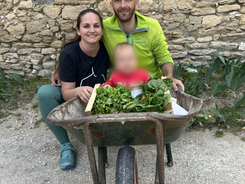 Hébergement en gîte rural, couple souriant avec un enfant et des légumes dans une brouette.