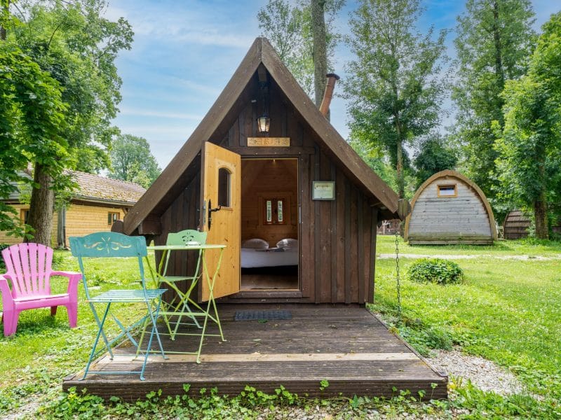 Cabane en bois à Champagne-Ardenne, avec chaises colorées et verdure environnante.