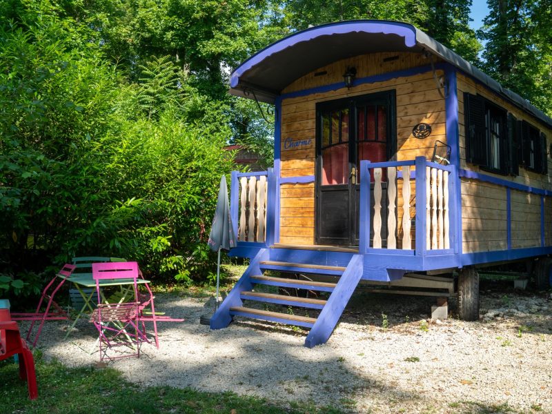 Charmante roulotte en bois à Champagne-Ardenne, entourée de verdure et de mobilier coloré.
